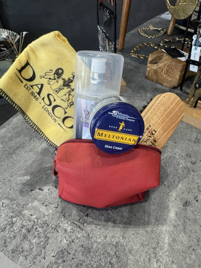 Red pouch with shoe care products including a can of 'Mellonian' and a wooden shoe brush on a gray surface.